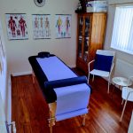A treatment room with massage couch seating area and medical posters on the walls ELEMENTAL SOLES